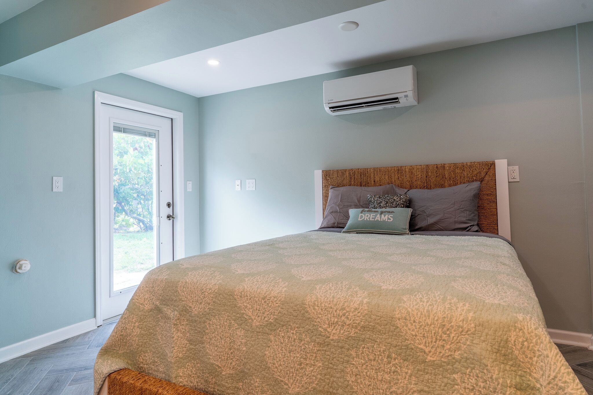 A bedroom with a bed, a door, an air conditioning unit, and a view through the door.