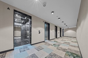 A hotel corridor with an elevator, carpeted floor, and a ceiling with recessed lighting. - Eurovea Tower, Danube View, Balcony & Parking (Ružinov)