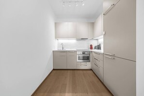 A modern kitchen with white cabinets, a stainless steel oven, and a wooden floor. - Eurovea Tower, Danube View, Balcony & Parking (Ružinov)