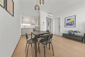 A modern kitchen with white cabinets, a dining table with four chairs, and pendant lighting. - Eurovea Tower, Danube View, Balcony & Parking (Ružinov)