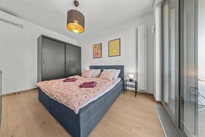 A modern bedroom with a bed, a bedside table, a wardrobe, and a large window. - Eurovea Tower, Danube View, Balcony & Parking (Ružinov)