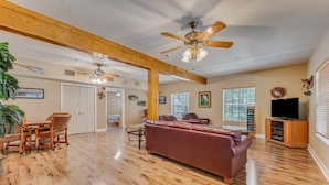 A spacious living room with a wooden ceiling, a large sofa, a dining table with chairs, and a television.