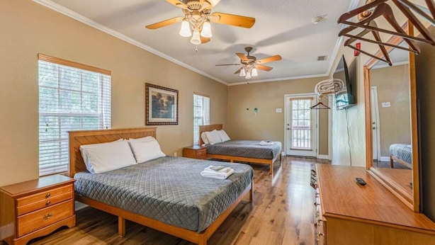 A bedroom with two beds, wooden floors, ceiling fans, and a wooden dresser.