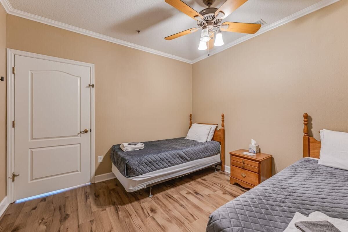 A bedroom with two beds, a wooden nightstand, a ceiling fan, and a door.