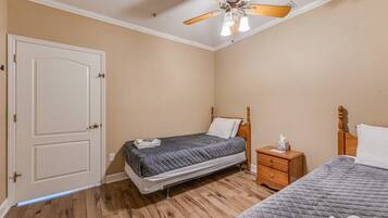 A bedroom with two beds, a wooden nightstand, a ceiling fan, and a door.