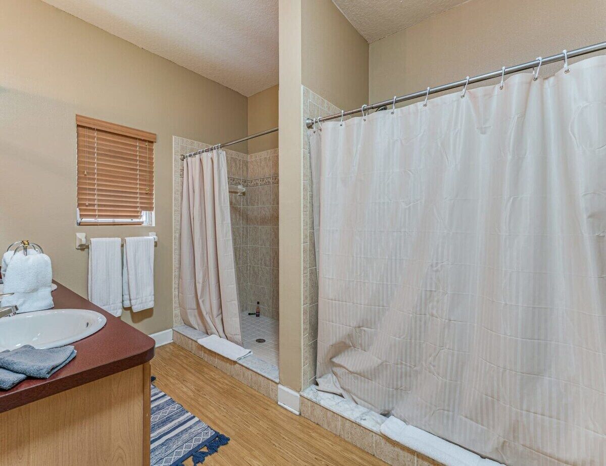 Baño con ducha, lavamanos y ventana con persianas.