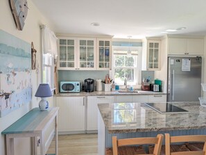 A kitchen with white cabinets, a granite countertop, a microwave, a refrigerator, and a window with curtains. - Quaint property right in town (New Shoreham)