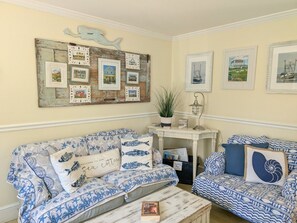 A cozy living room with two patterned sofas, a coffee table, and a wall decorated with framed pictures and a rustic board. - Quaint property right in town (New Shoreham)