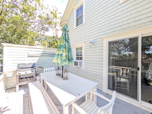 A patio with a grill, white wooden table, and chairs, and a sliding glass door leading to a deck. - Quaint property right in town (New Shoreham)