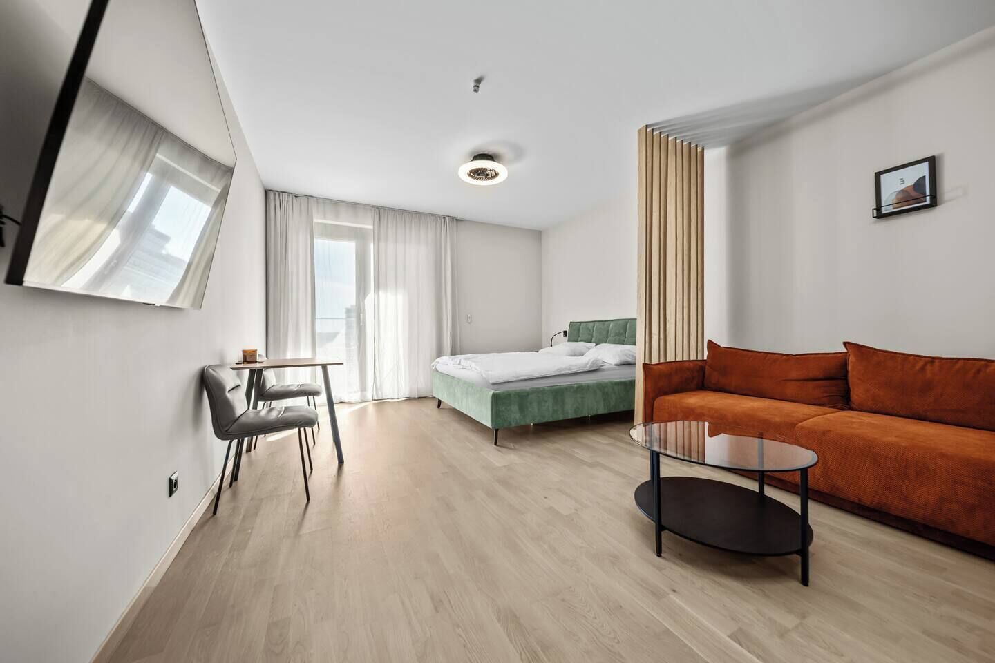 A modern hotel room with a bed, a sofa, a dining table, and a chair.