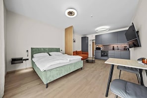 A modern hotel room with a bed, a desk, a chair, a television, and a kitchenette. - Metropolis Downtown, Balcony, AC & Free Parking (Bratislava)