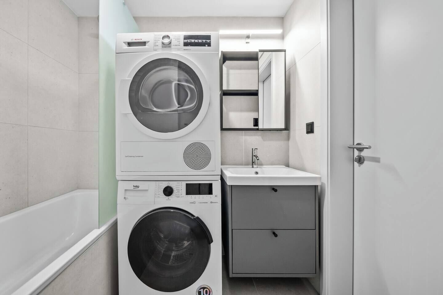 Ein kleiner Hauswirtschaftsraum mit Waschmaschine, Trockner, Spüle und Spiegel.