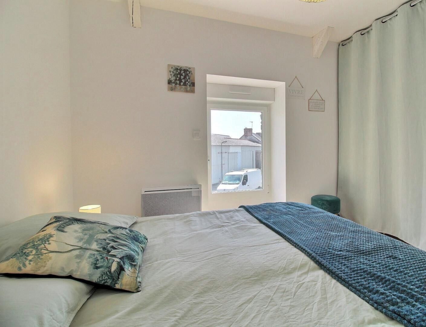 Une chambre à coucher avec un lit, une lampe de chevet, un radiateur et une vue sur l’extérieur.