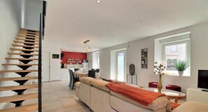 A modern interior with a staircase, a dining area, and a living room with a sofa and a TV. - Le Cocon du Bourg - BAULON (BAULON)