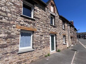 A stone building with multiple windows and doors, a paved sidewalk, and a clear sky. - Le Cocon du Bourg - BAULON (BAULON)