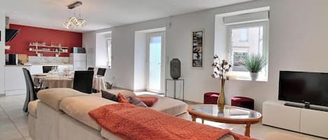 A modern living room with a sofa set, a television, and a dining area with a table set for four.