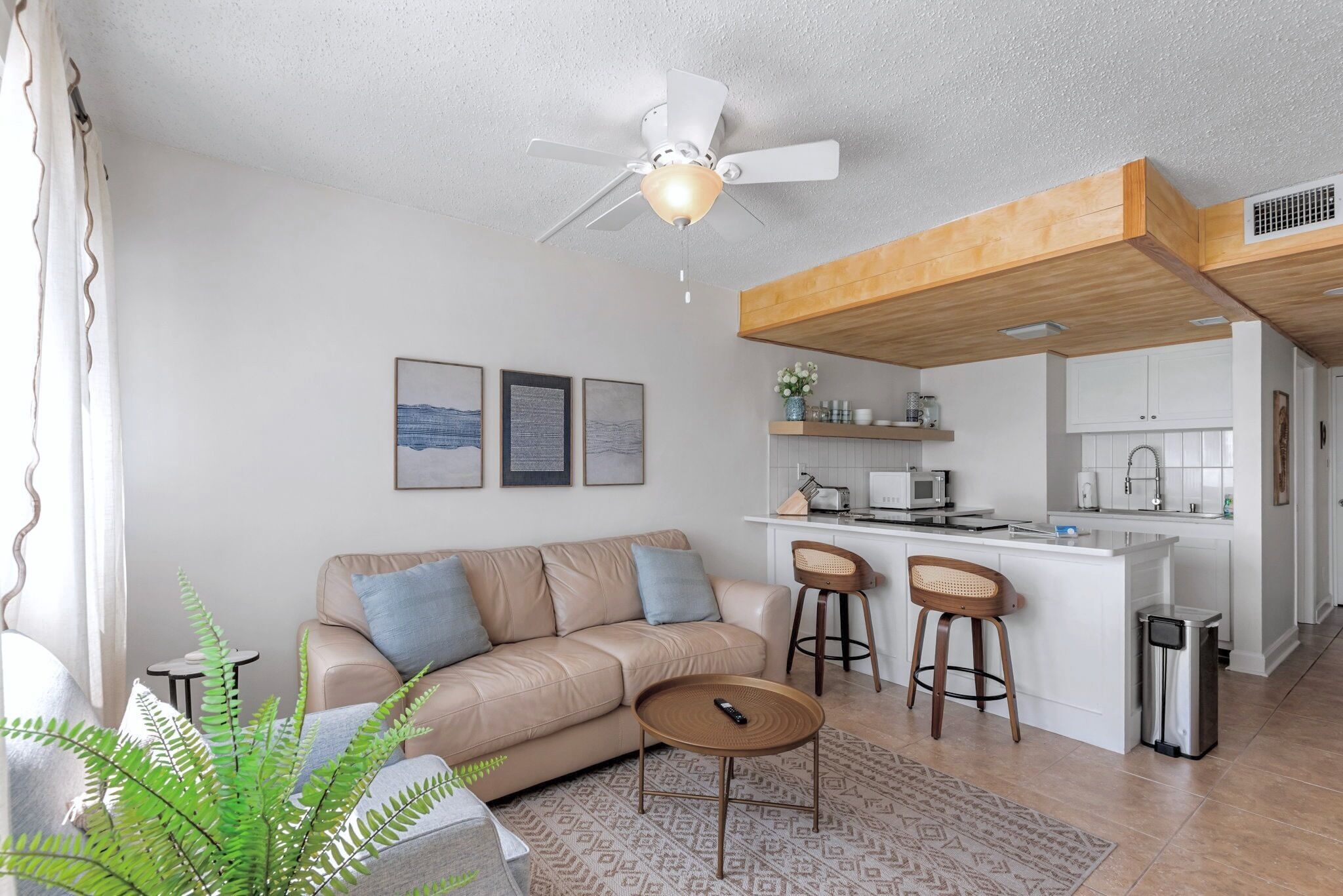 A modern living room with a sofa, coffee table, and a small kitchen area with a bar stool.