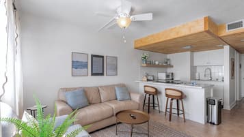 A modern living room with a sofa, coffee table, and a small kitchen area with a bar stool.