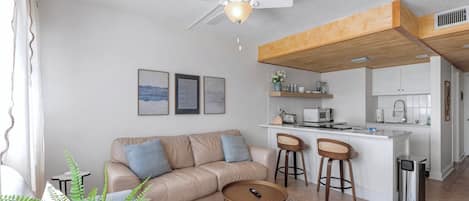 A modern living room with a sofa, coffee table, and a small kitchen area with a bar stool.