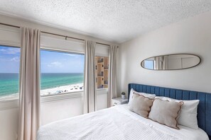 Quarto de hotel com cama, mesa de cabeceira, espelho e vista para a praia.