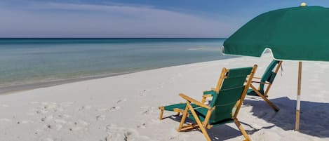 Una playa con dos sillas de madera y una sombrilla verde.
