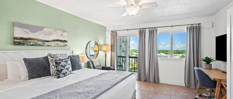 A hotel room with a bed, a desk, a chair, a ceiling fan, and a view through the window.