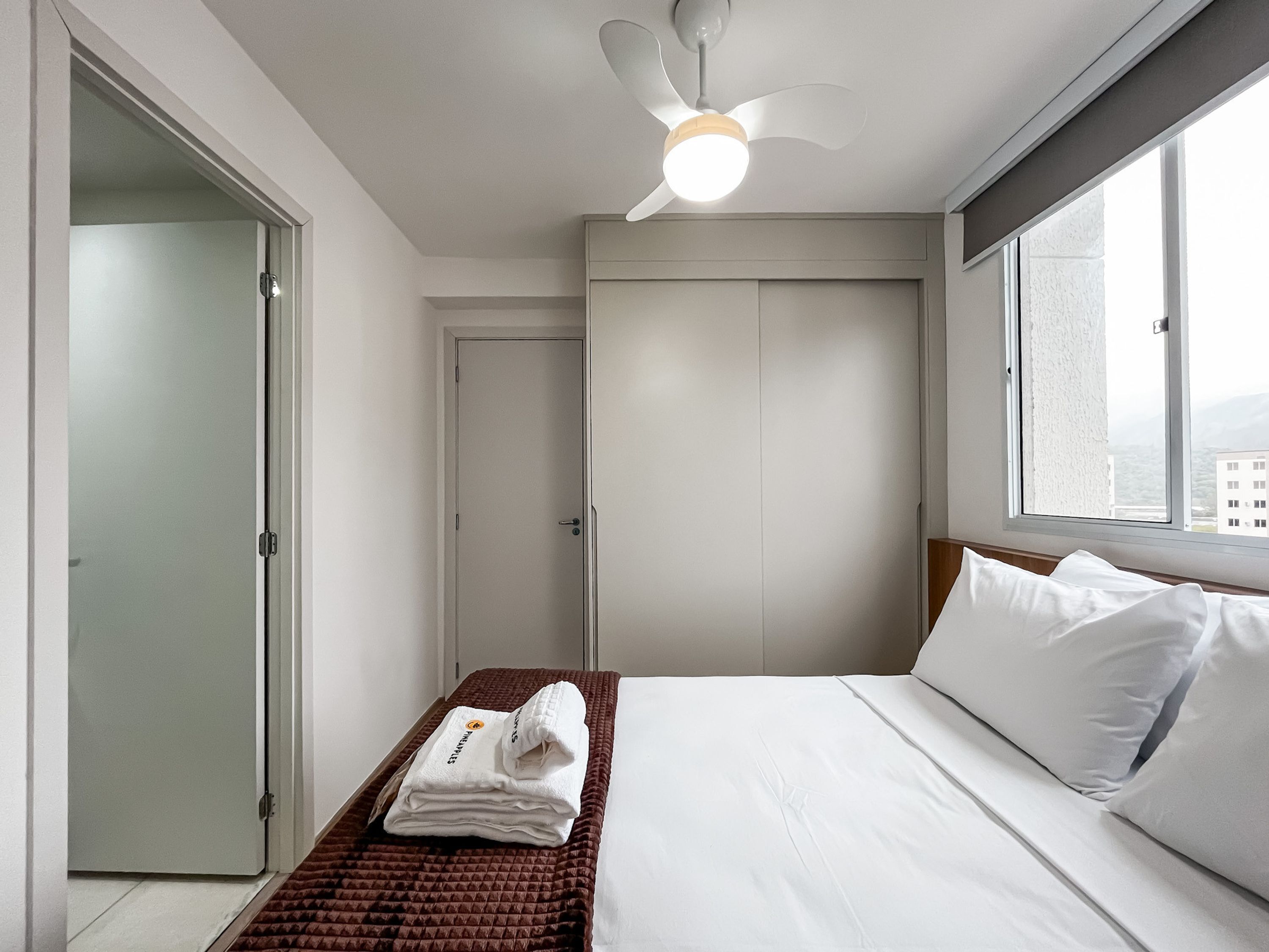 Una habitación de hotel con una cama, una ventana, un ventilador de techo y una puerta.