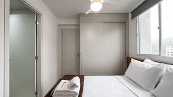 A hotel room with a bed, a window, a ceiling fan, and a door.