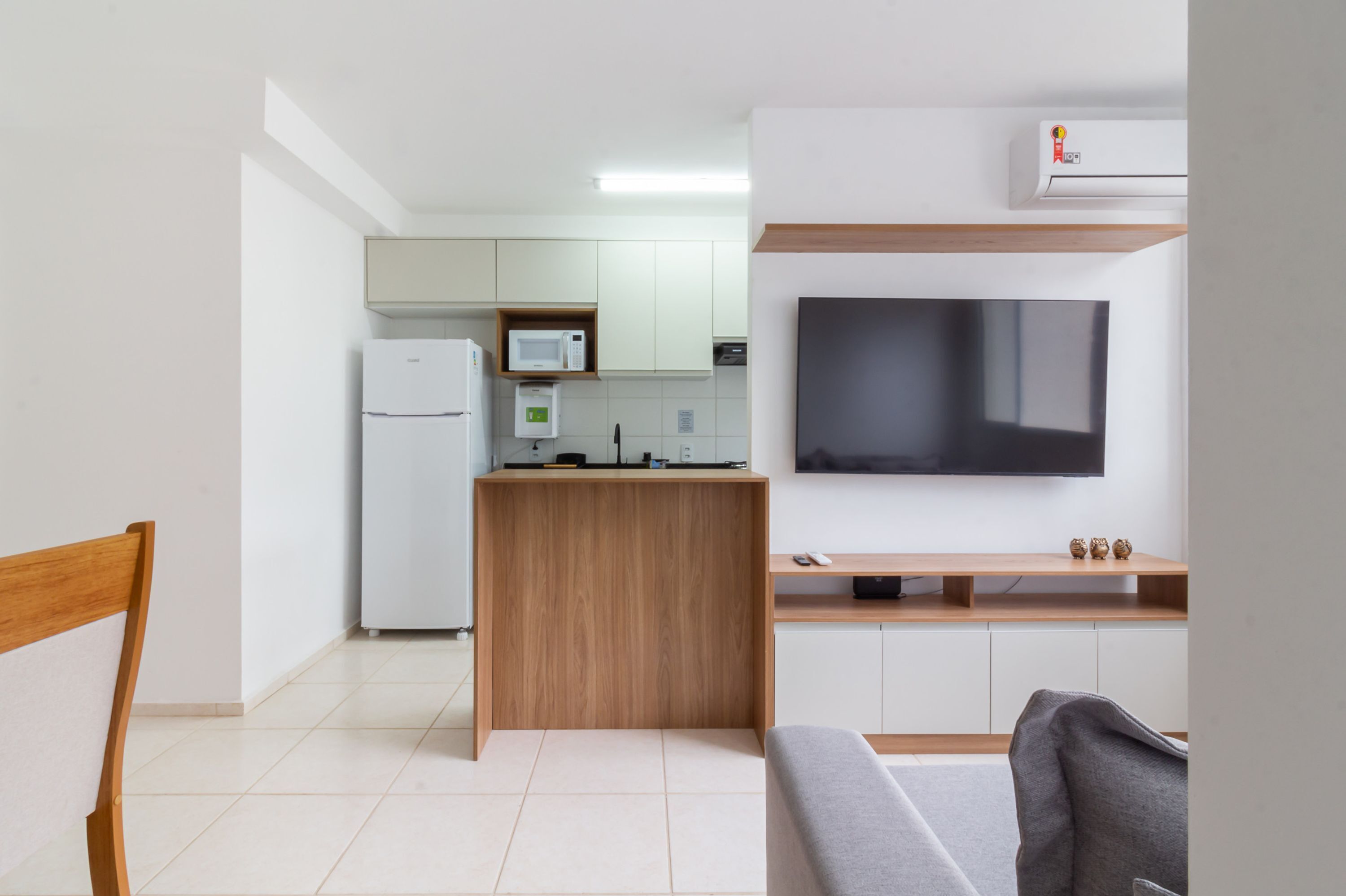 A compact kitchen with a refrigerator, microwave, and a small island. A flat-screen TV is mounted on the wall above a wooden counter.