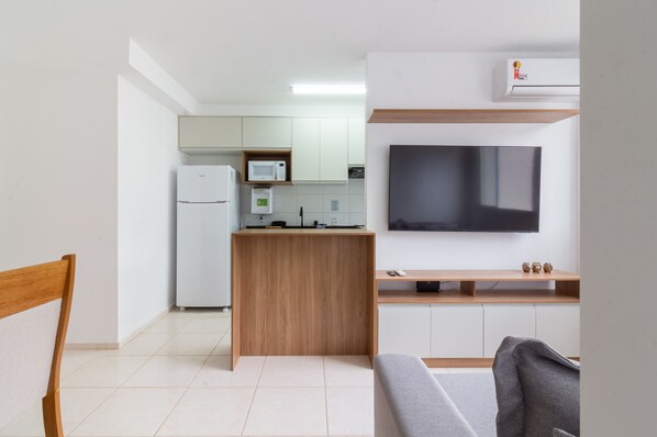 A compact kitchen with a refrigerator, microwave, and a small island. A flat-screen TV is mounted on the wall above a wooden counter.