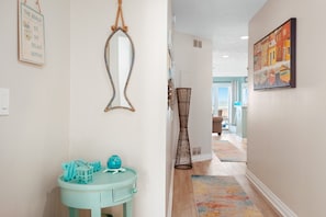 A hallway with a light blue vanity, a mirror, a framed sign, a black vase, and a colorful rug leading to a room with a view. - Coastal Duo 108 & 109 | Beachfront | Near Downtown + Tart Trail (Traverse City)