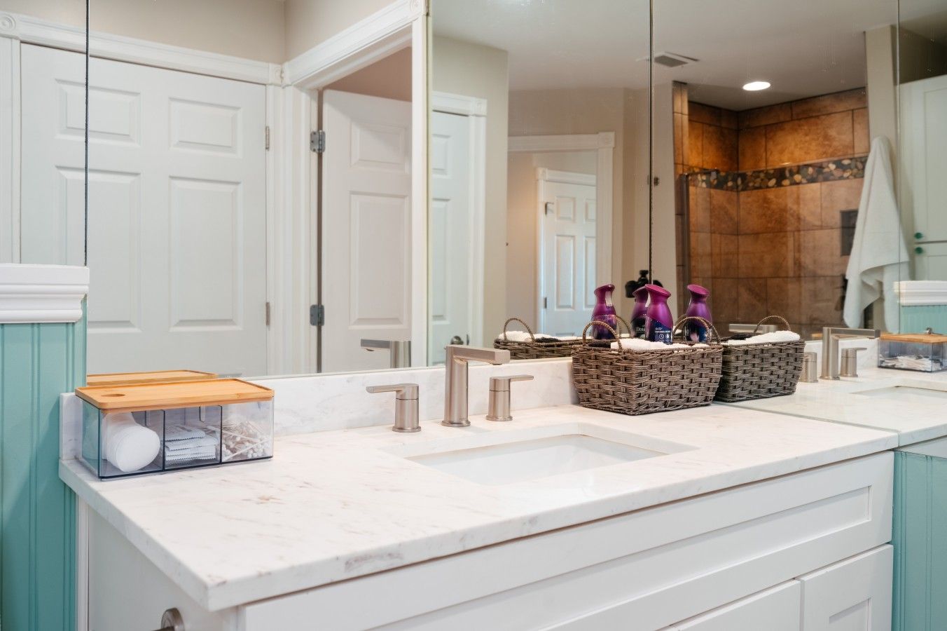 A bathroom with a double sink, a mirror, and wicker baskets on the counter.