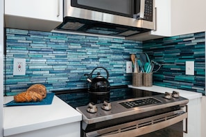A modern kitchen with a blue mosaic backsplash, a kettle, and a loaf of bread on the counter. - Coastal Duo 108 & 109 | Beachfront | Near Downtown + Tart Trail (Traverse City)