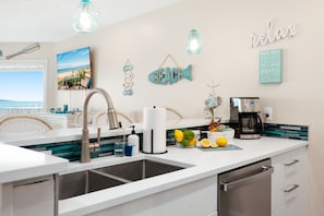 A modern kitchen with a large sink, a coffee maker, and a view of the beach. - Coastal Duo 108 & 109 | Beachfront | Near Downtown + Tart Trail (Traverse City)