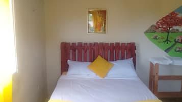 A bed with white and yellow bedding, a wooden headboard, a small table, and a painting on the wall.