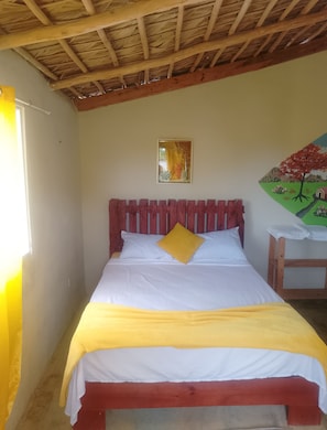 A bed with white and yellow bedding, a wooden headboard, a small table, and a painting on the wall.