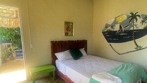 Ein Zimmer mit einem Bett, einer grünen Bank, einer Wand mit einem tropischen Wandbild und einem Reetdach.