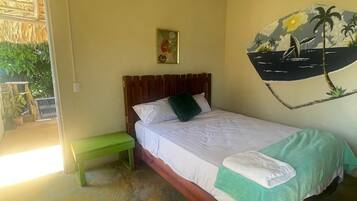A room with a bed, a green bench, a wall with a tropical mural, and a thatched ceiling.