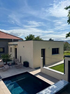 A modern outdoor pool area with a rectangular pool, lounge chairs, and a small building with a flat roof. - Les Nids des Mûriers (2-person) (CHAPAREILLAN)