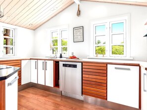 Eine moderne Küche mit Holzschränken, einem Geschirrspüler und einem Fenster mit Blick ins Grüne.
