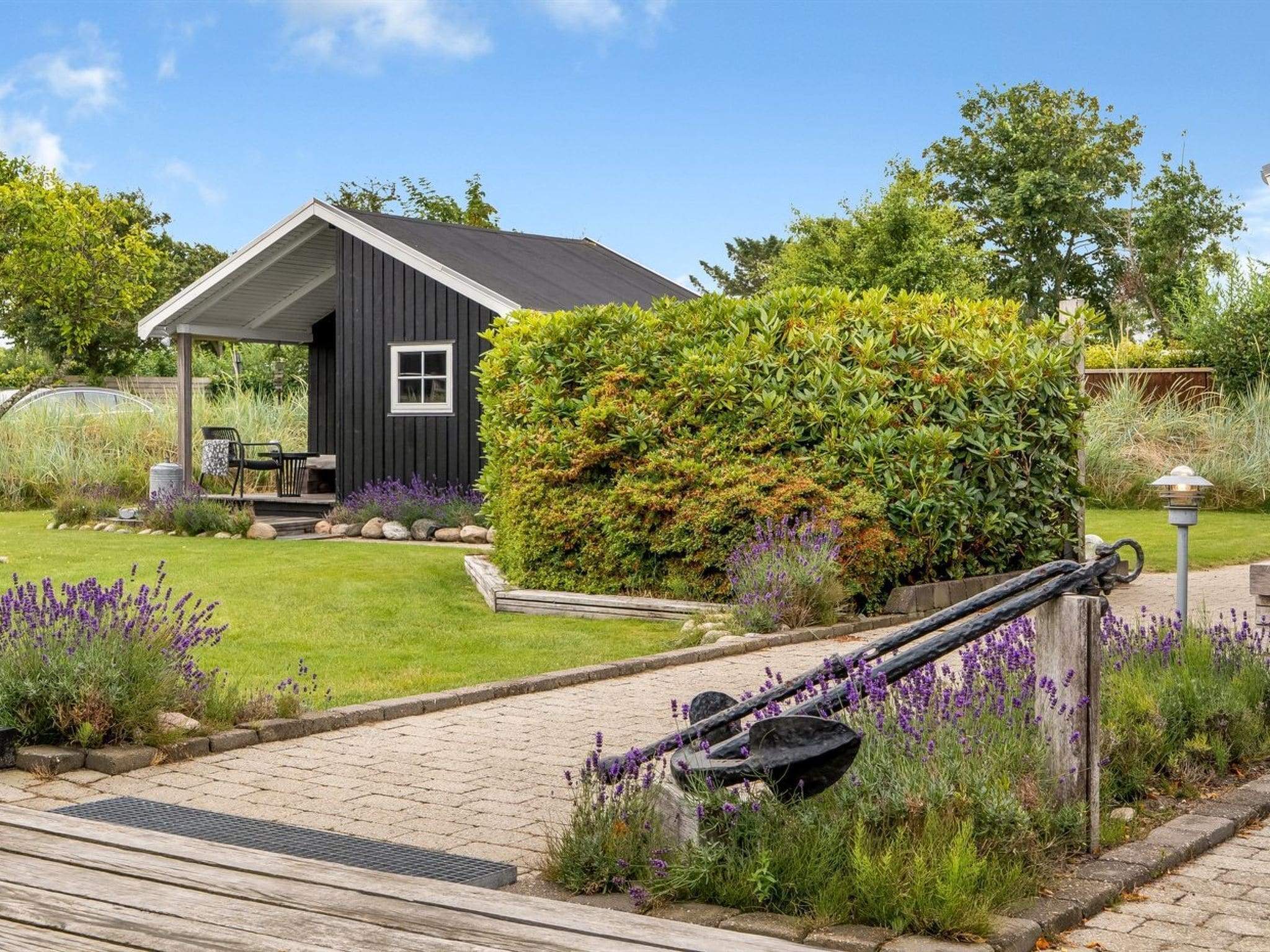 Ein schwarzes Holzhaus mit einer Veranda, umgeben von einem gepflegten Garten mit Lavendel und verschiedenen Sträuchern.