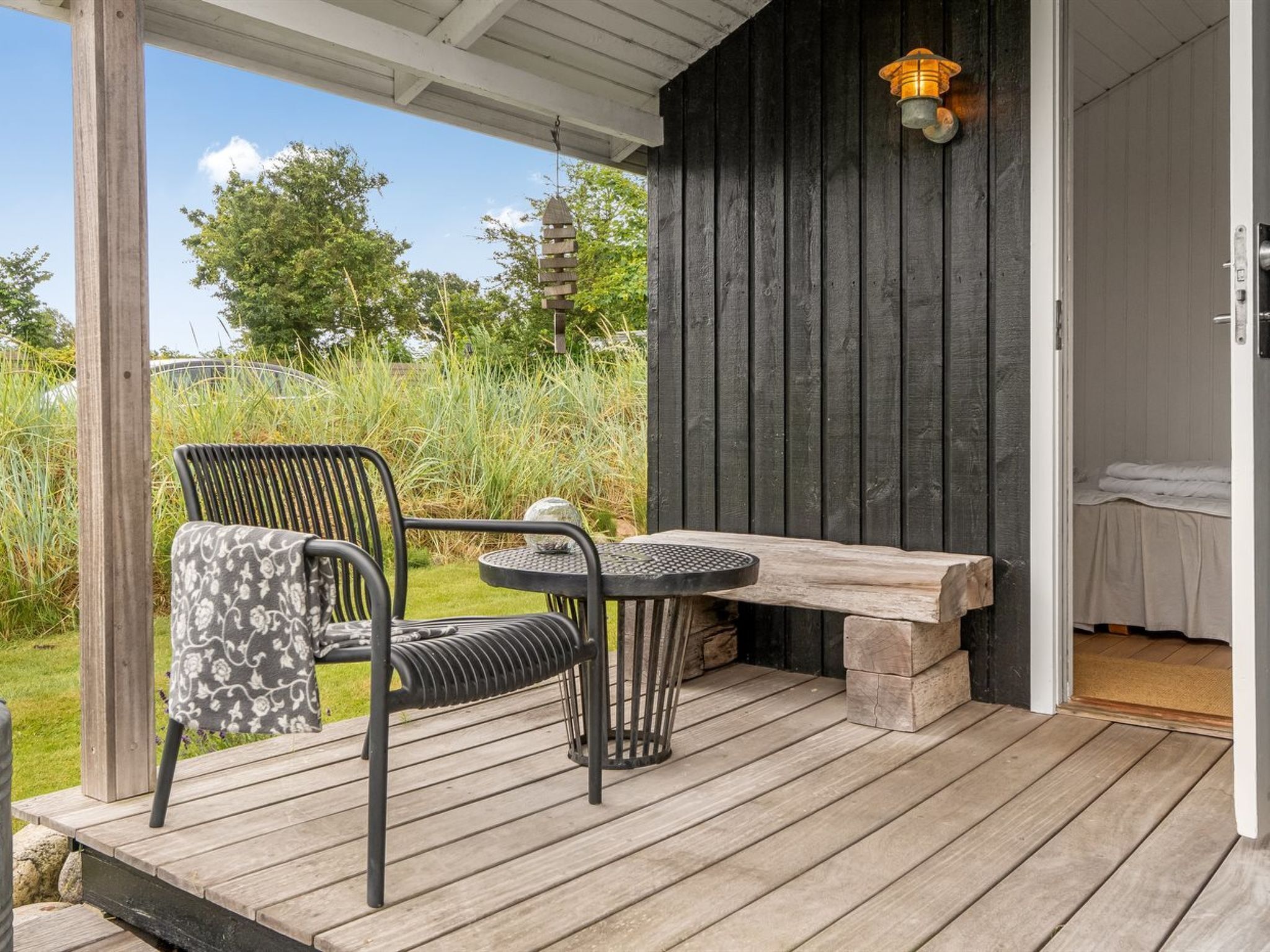 Una terraza de madera con una mesa y sillas metálicas, un banco y una puerta que da a un espacio interior.