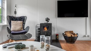 Ett modernt vardagsrum med en öppen spis, en bekväm fåtölj, en platt-TV och ett bord med material för stickning.