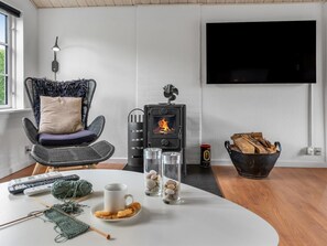 Ein modernes Wohnzimmer mit Kamin, einem bequemen Sessel, einem Flachbildfernseher und einem Tisch mit Strickzeug.