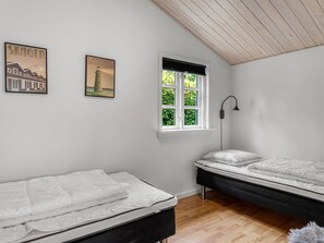 A bedroom with two beds, a window with blinds, and two wall-mounted pictures.