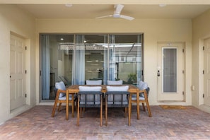A covered patio with a table and chairs, a ceiling fan, and a sliding glass door leading to a covered area. - 5BR Kissimmee | Pool & Lazy River | 13 Min Disney (Kissimmee)