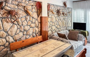 A living room with a stone wall, a wooden bench, a sofa, and a television. - Stunning apartment in Lopar with house sea view (Lopar)