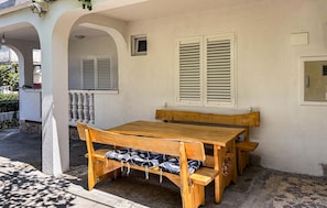 A wooden table and bench set against a white wall with shutters, under a covered patio area. - Stunning apartment in Lopar with house sea view (Lopar)