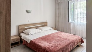 Un dormitorio con cabecera de madera, cama con ropa de cama blanca, mesita de noche y una ventana con cortinas.