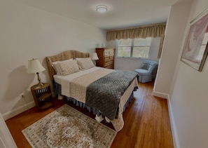 A bedroom with a bed, bedside table, lamp, dresser, chair, and a window with curtains. - Perfect 5-bedroom house with AC in delightful Newport (Newport)